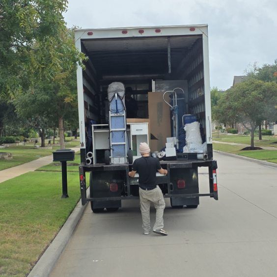 Stacked moving boxes in a truck during a house move, with furniture and a ladder nearby.
