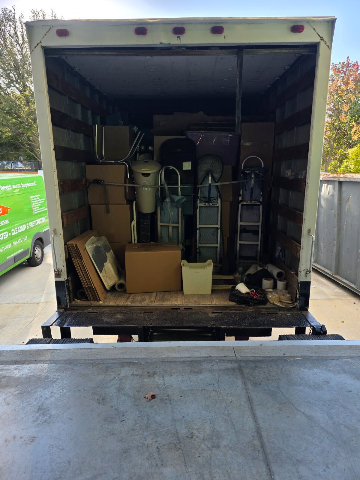 Two movers in blue shirts lifting a TV in a room with stacked moving boxes