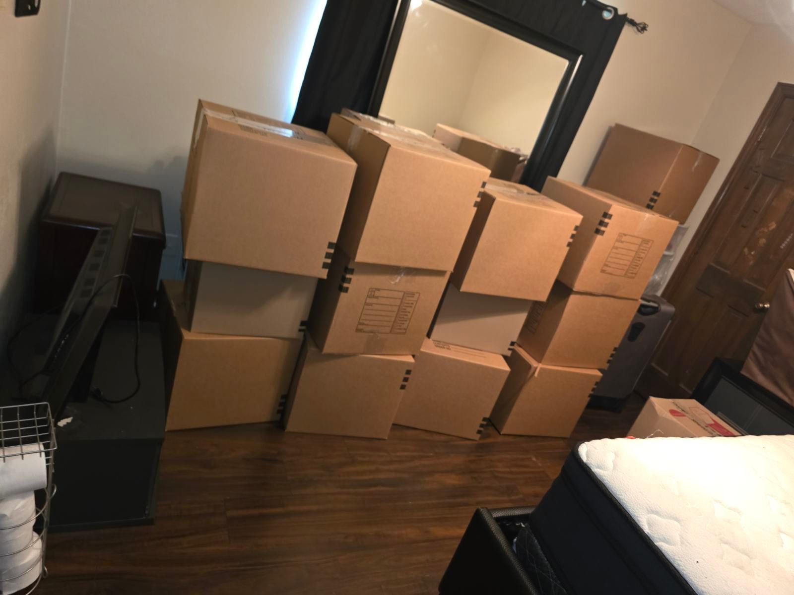 Person packing a cardboard box with a tape dispenser in a room full of moving boxes