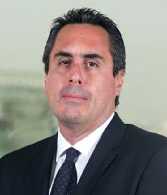 A man in a suit and tie is standing in front of a window.