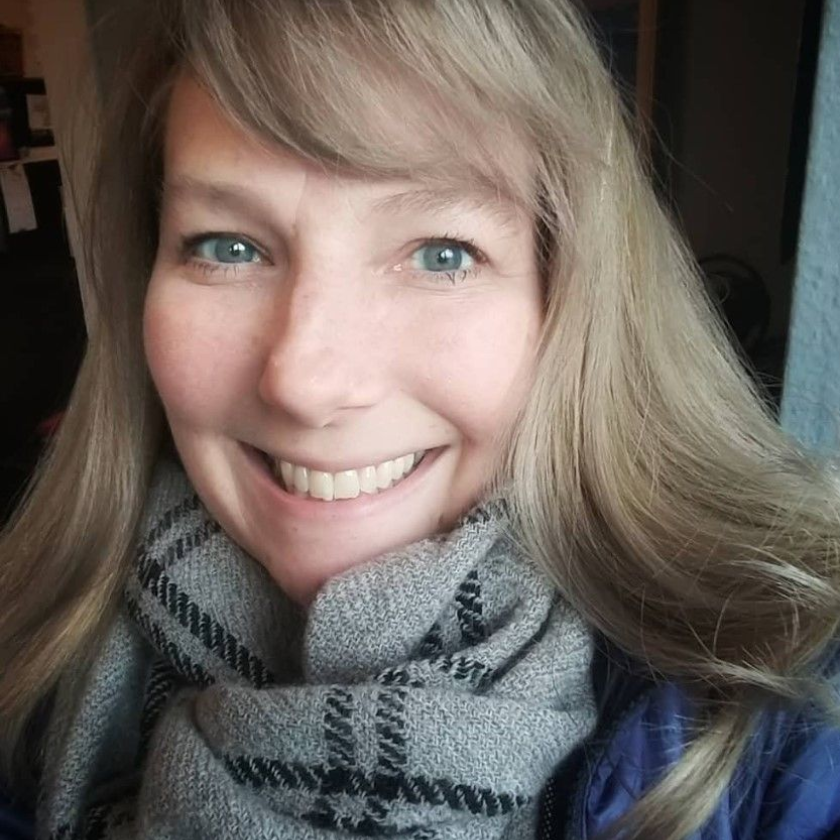 Woman with blonde hair and scarf smiles at the camera.