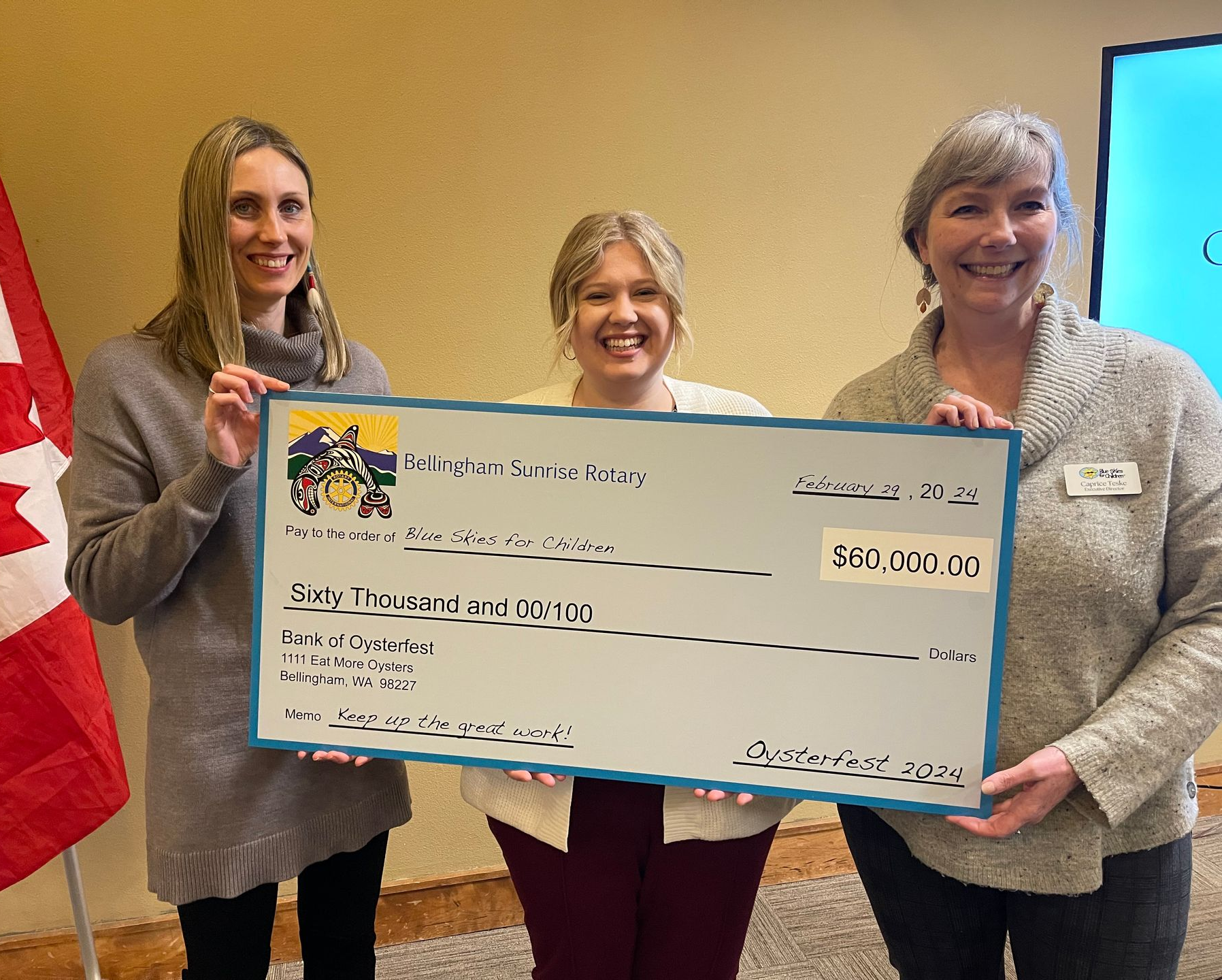 Three people holding a large check for $60,000.00. Canadian flag in background.