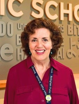 Woman with curly brown hair, red shirt, smiling, standing in front of a sign.