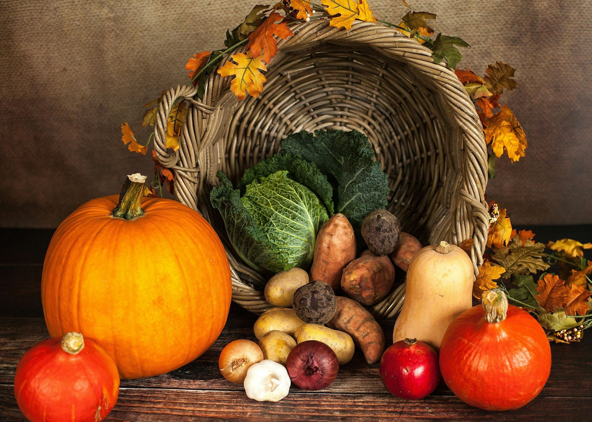 A cornucopia overflowing with autumn harvest produce: pumpkins, squash, cabbage, and root vegetables.