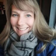 Woman with blonde hair and a gray scarf smiling at the camera.