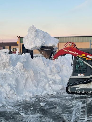 Snow removal with a red Takeuchi track loader, scooping a large pile of snow.