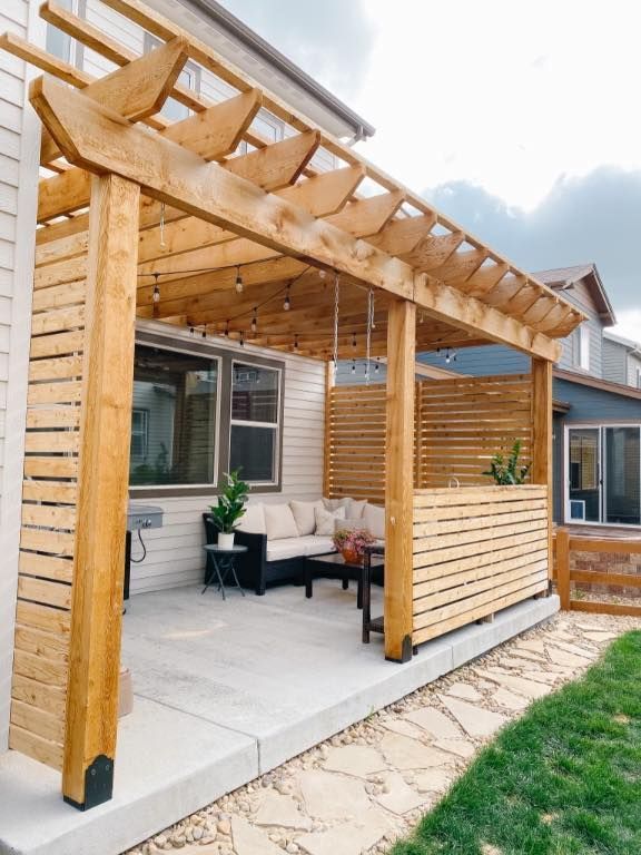 Backyard patio with fire pit, bordering a large house with two levels and a deck. Green grass and overcast sky.