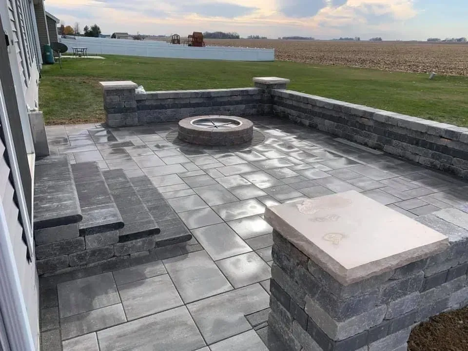 Patio with gray pavers, built-in fire pit, and retaining walls, in a backyard setting.