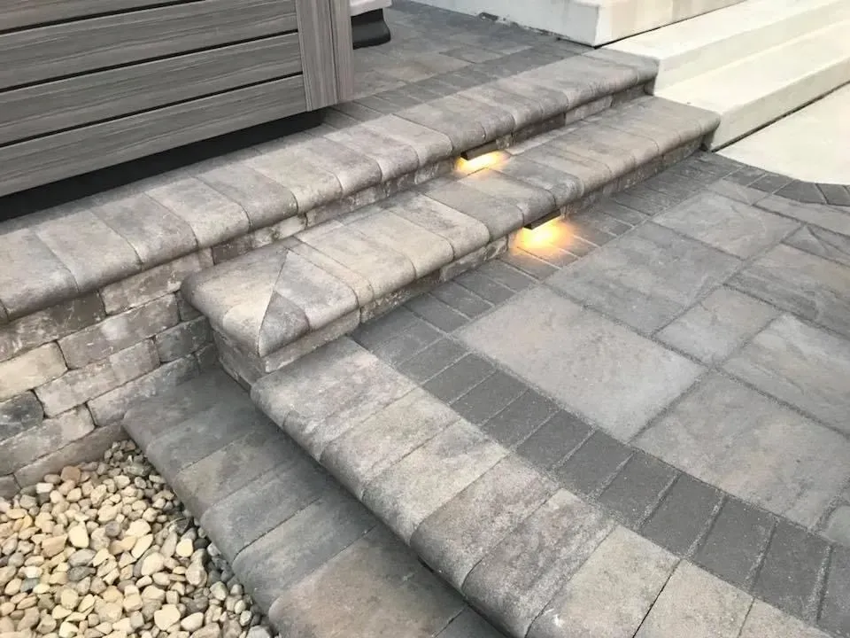Stone steps with built-in lights leading to a raised patio area, surrounded by brick and gravel.