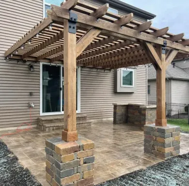 Wooden pergola over brick patio outside a beige house.