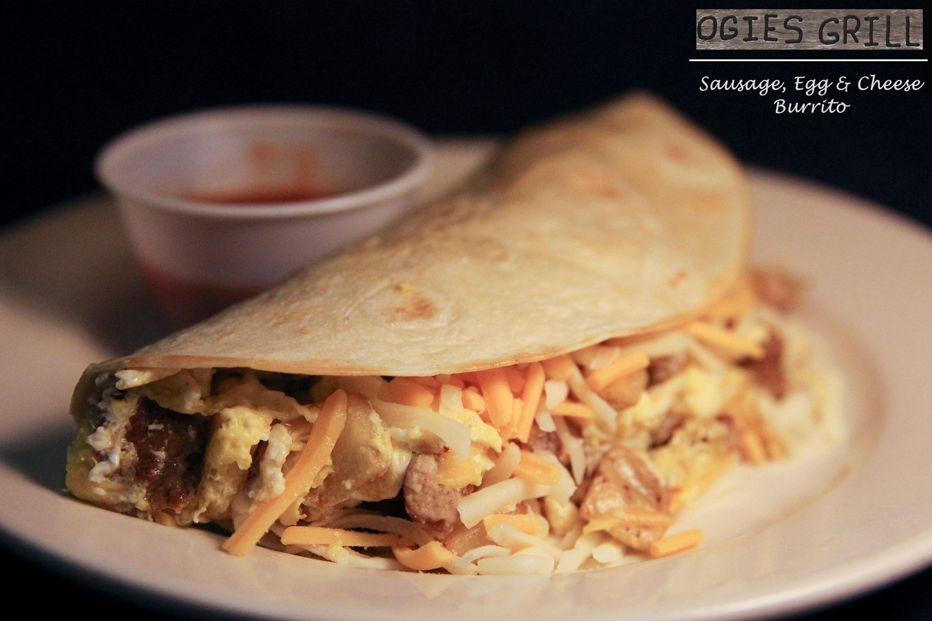 A white plate topped with a burrito and dipping sauce from ogies grill
