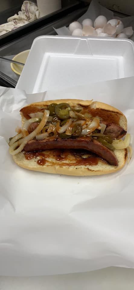 A hot dog with onions and peppers on a bun is sitting on a styrofoam container.