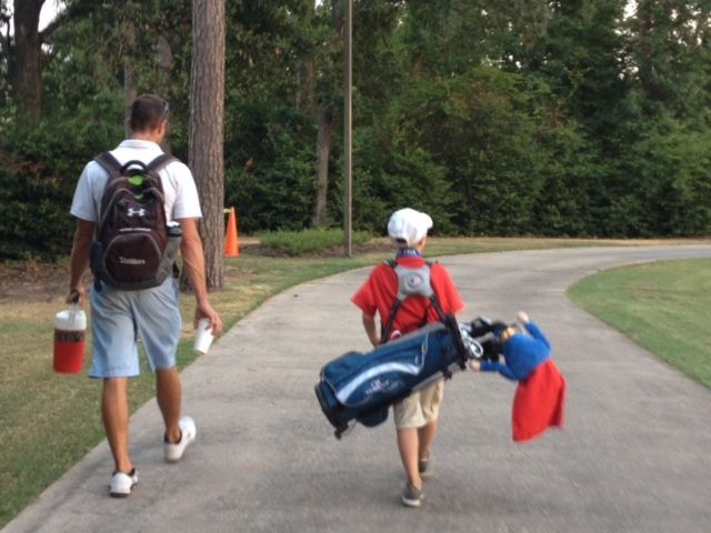 A man and a boy are walking down a path carrying golf bags