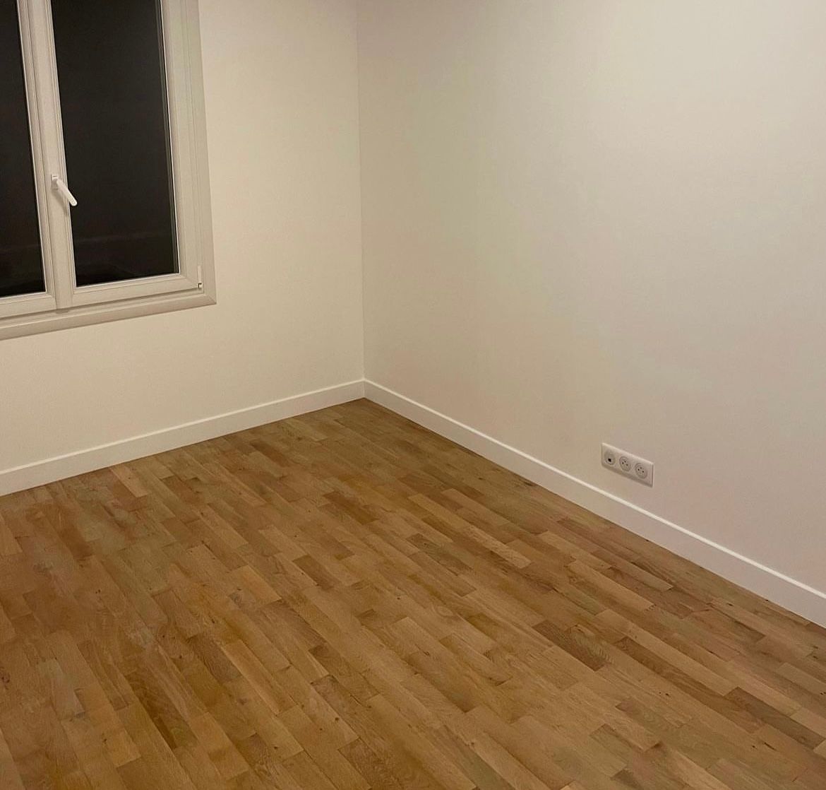 une pièce vide avec du parquet et des murs blancs.