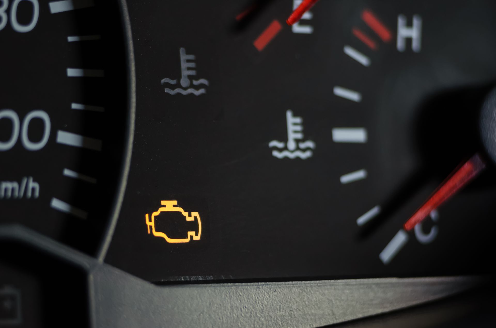 Close-up of a car dashboard; illuminated check engine light is visible, indicating a potential engine issue.