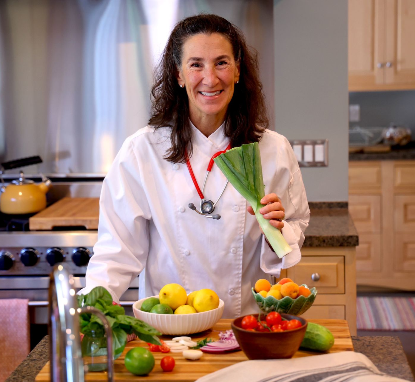 Woman in chef coat with stethoscope, smiling in a kitchen setting.