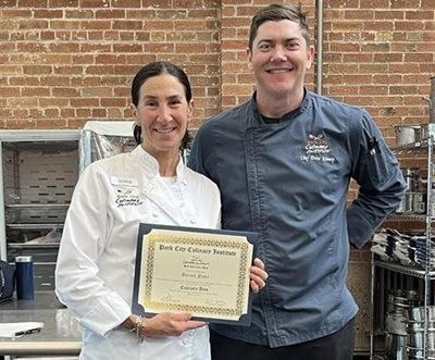 Two chefs smiling, holding a certificate in a kitchen.