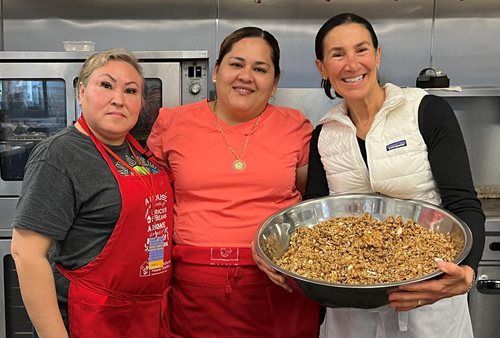 Three women in a kitchen, one holding a bowl of granola. They are smiling.
