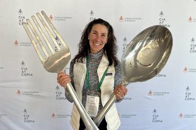 Woman smiling, holding giant fork and spoon in front of a CIA at Copia backdrop.