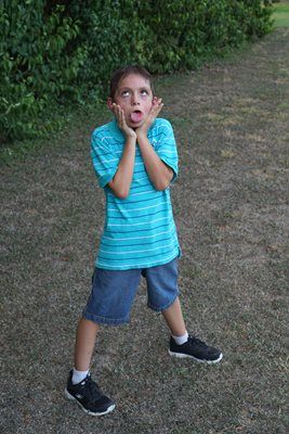 Boy making a silly face, sticking out tongue, hands on cheeks, outdoors.