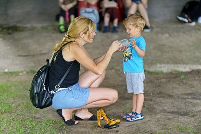 Woman giving a small boy a water bottle, outdoors. He wears a blue shirt and gray shorts.