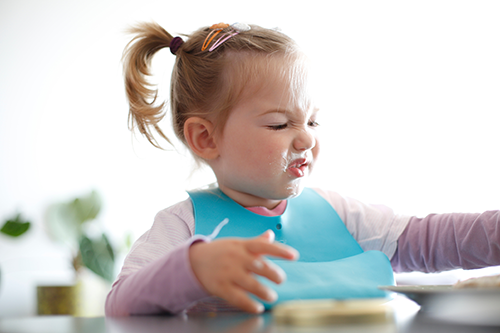 Toddler wearing bib, making a disgusted face, smeared food on face.