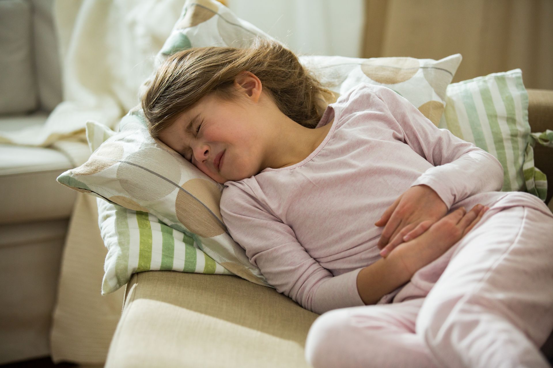 Sleeping person resting on a couch with a pillow, wearing light pink pajamas and a white blanket