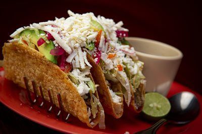 Three loaded tacos on a red plate with a lime wedge and a small bowl.