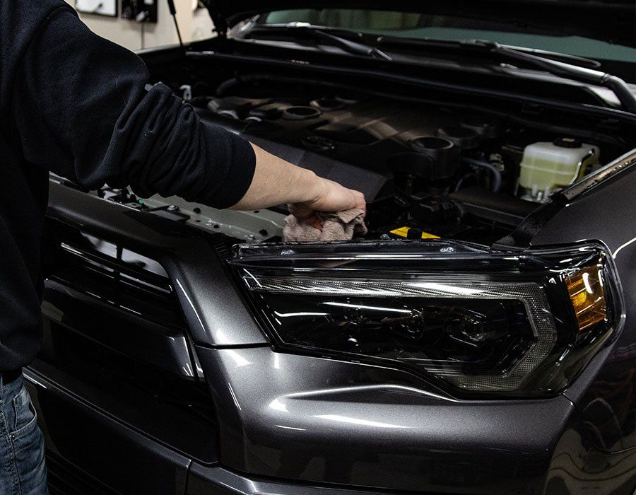 Person cleaning the engine of a dark gray car, under the hood.