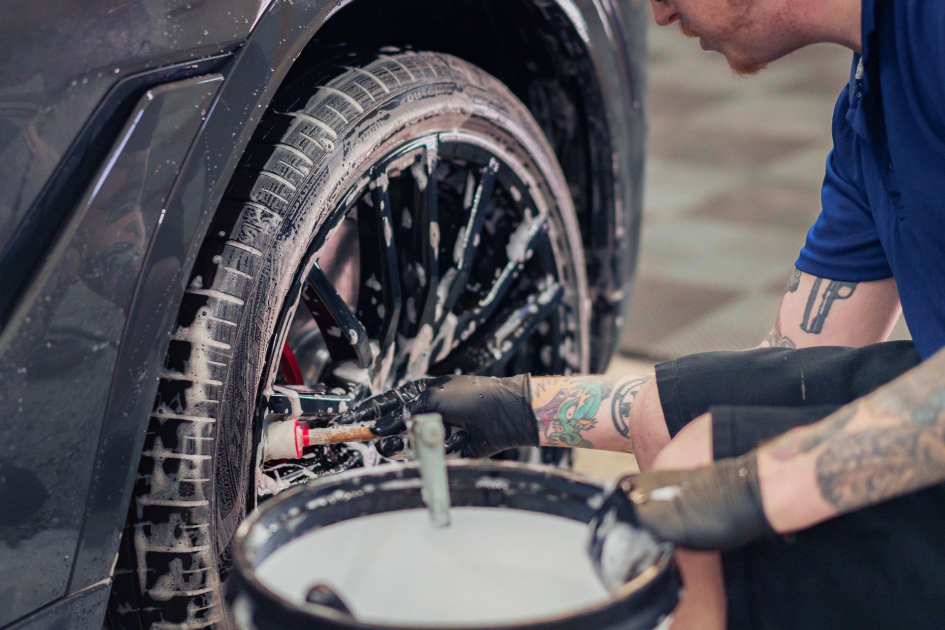 Person washing a car tire with a brush and soapy water.