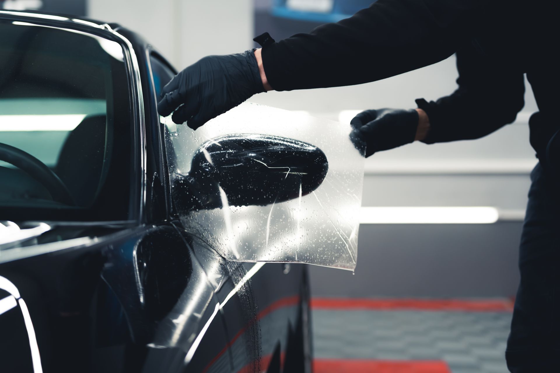 A man is applying a protective film to the side mirror of a car.