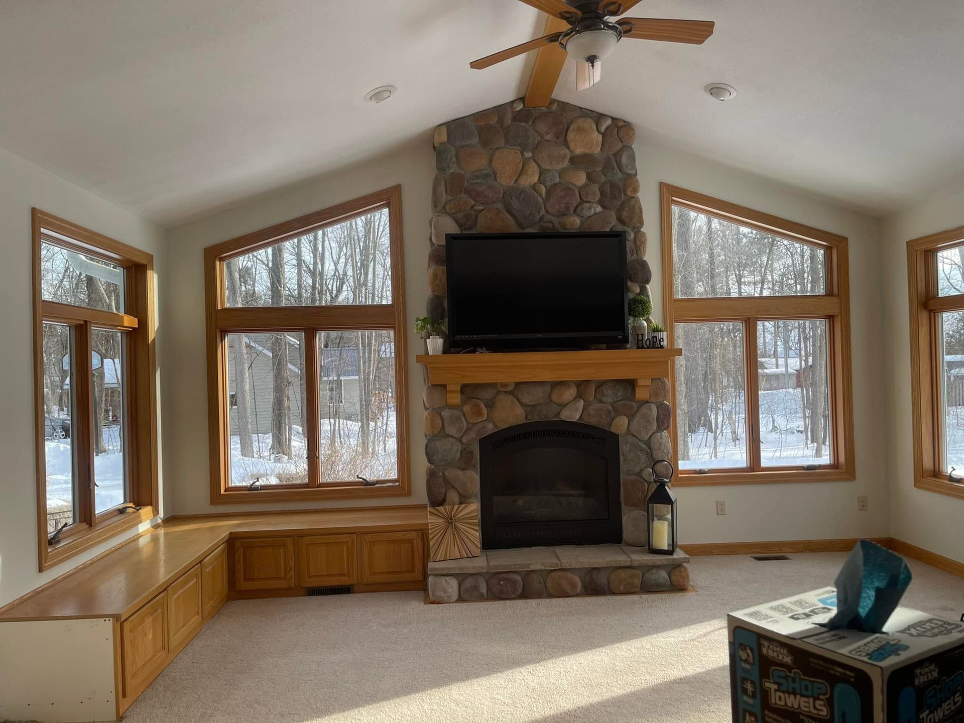 Bright living room with stone fireplace, large windows, built-in benches, and a ceiling fan.