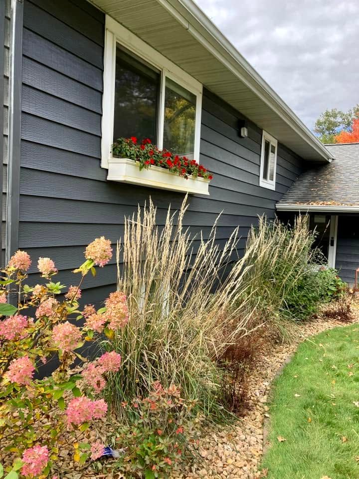 Dark gray house exterior with a flower box and a landscaped garden of tall grasses and pink flowers.