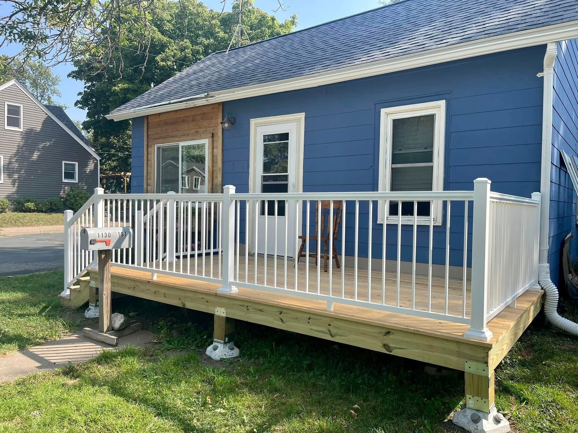 Blue house with a small wooden front porch and white railing in a grassy yard