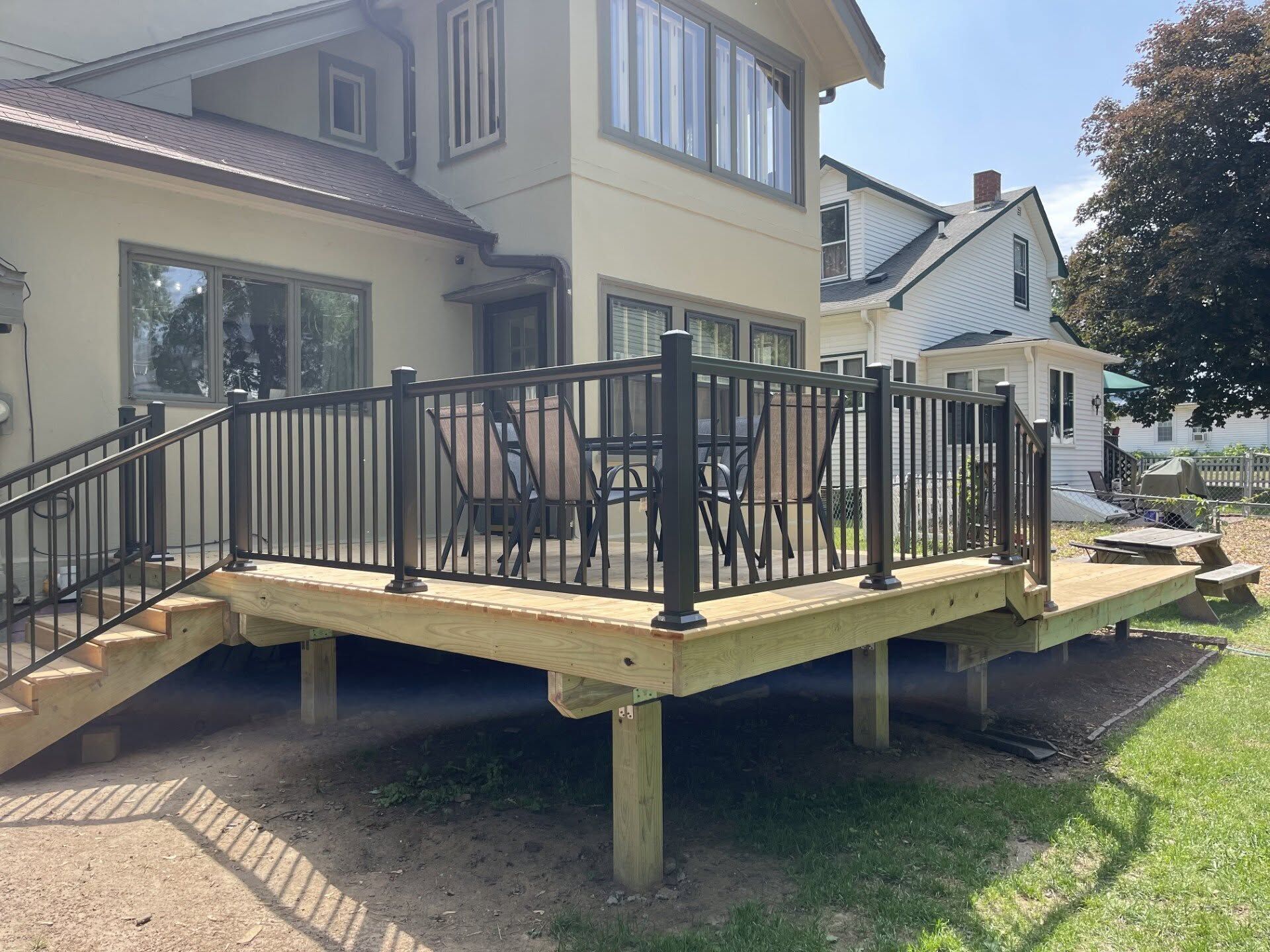 Raised wooden deck with black metal railing beside a house in a backyard.