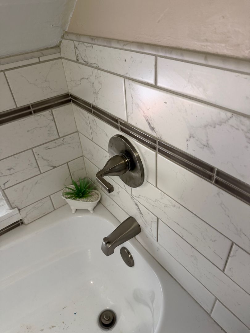 White tiled bathroom sink with chrome faucet, small potted plant, and a wall-mounted soap dish.