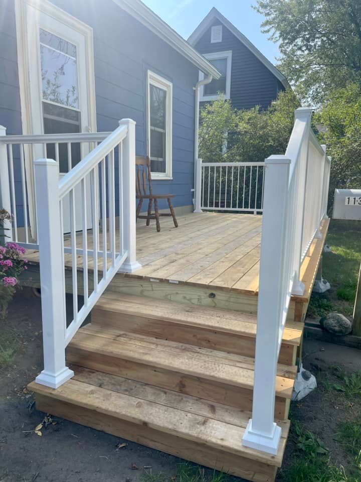 Blue house porch with wooden deck, white railings, and three front steps leading up to it