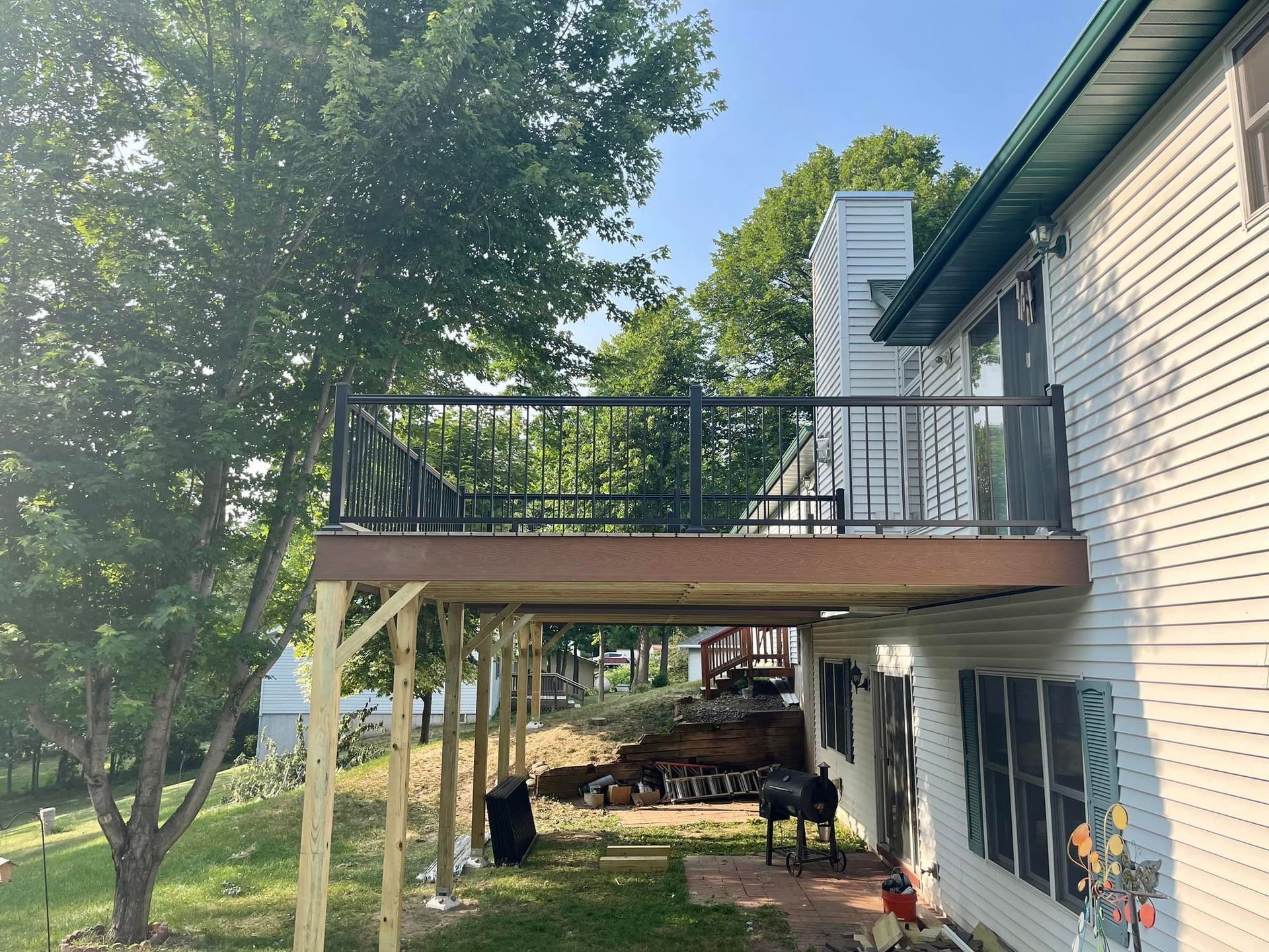 Back deck on a house with black railing, white chimney, and shaded yard below