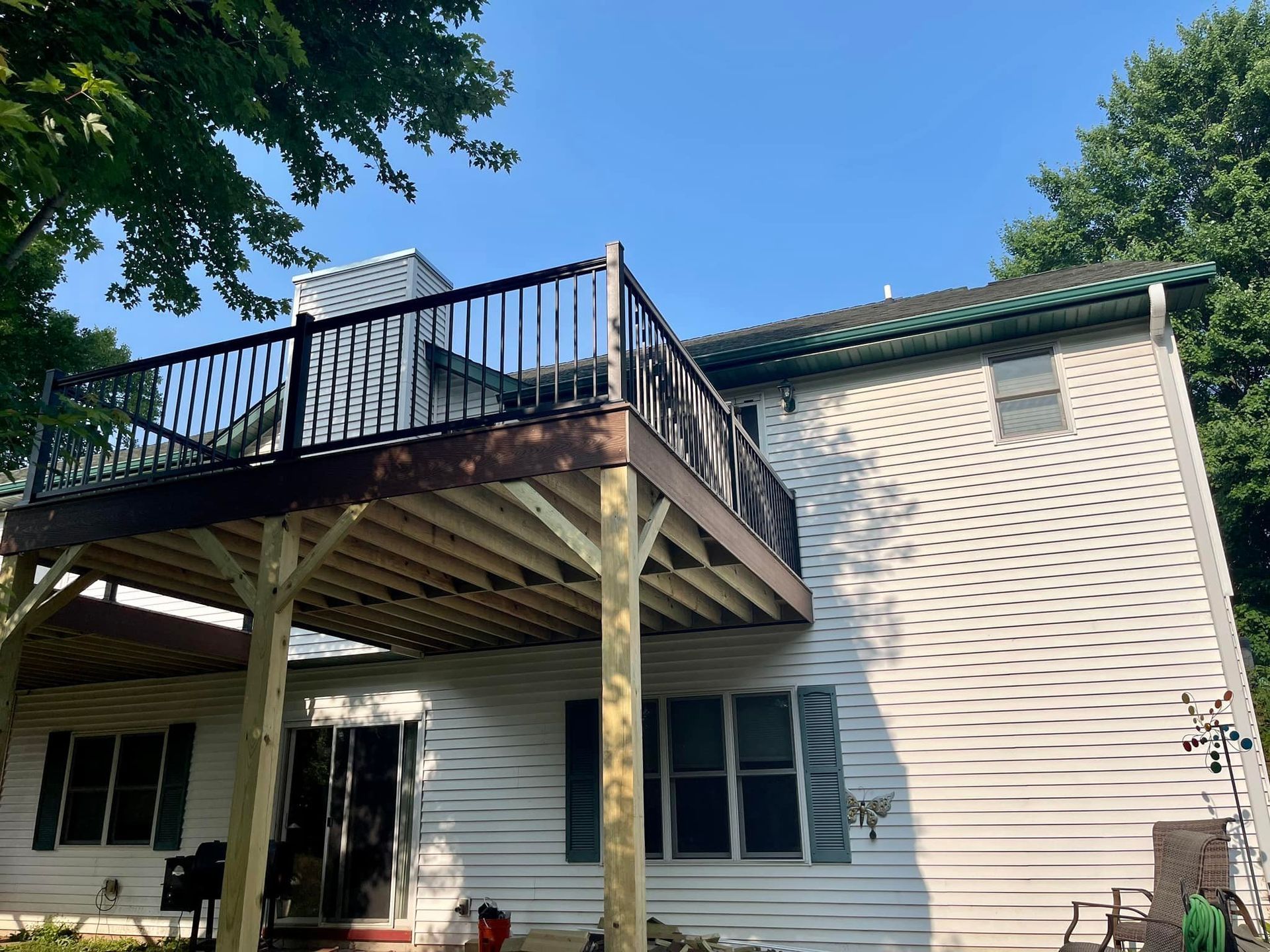 Back deck on a white house with black railing and support posts under a clear blue sky
