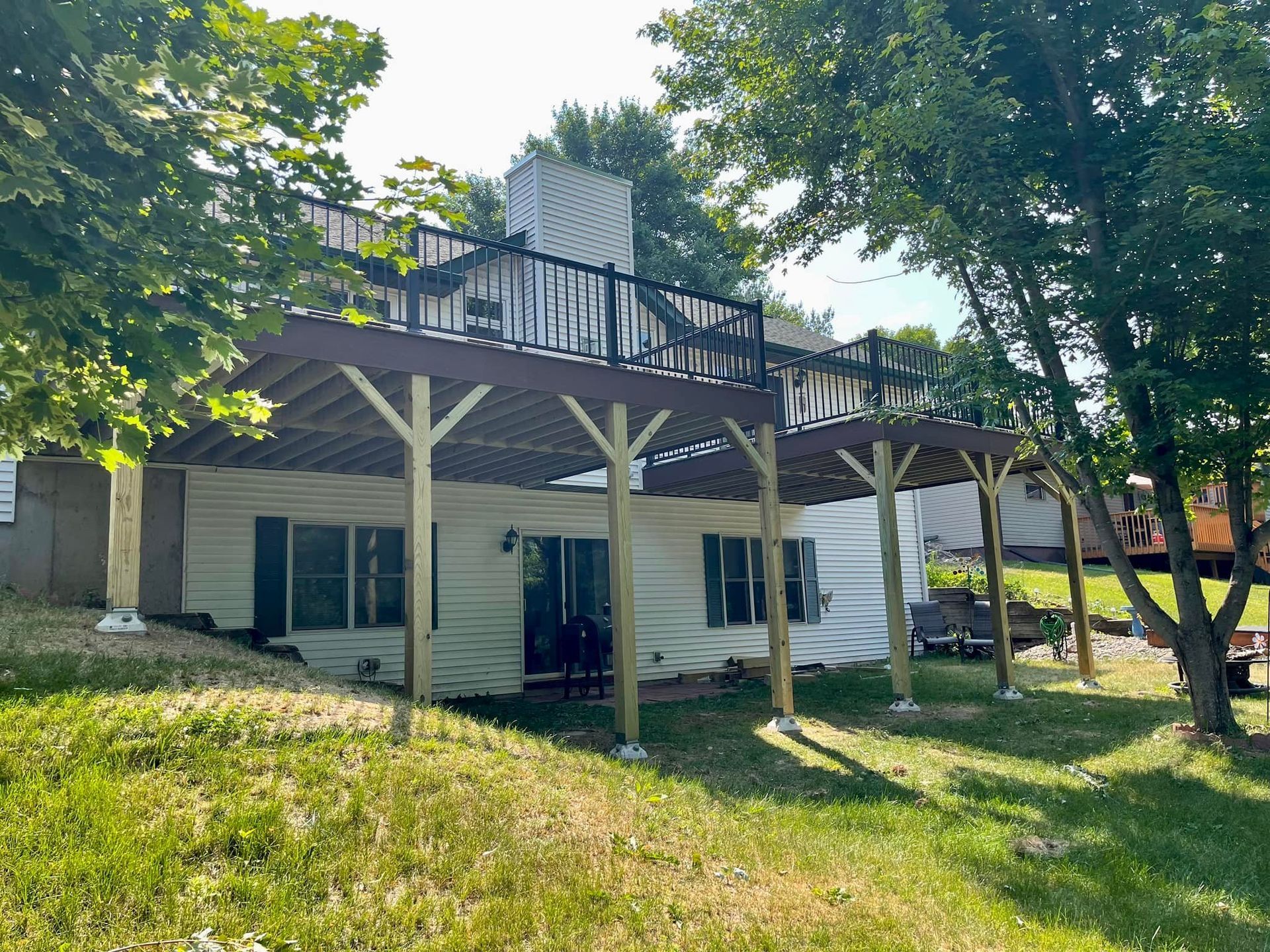 Backyard house with a raised wooden deck, white posts, and trees in the foreground