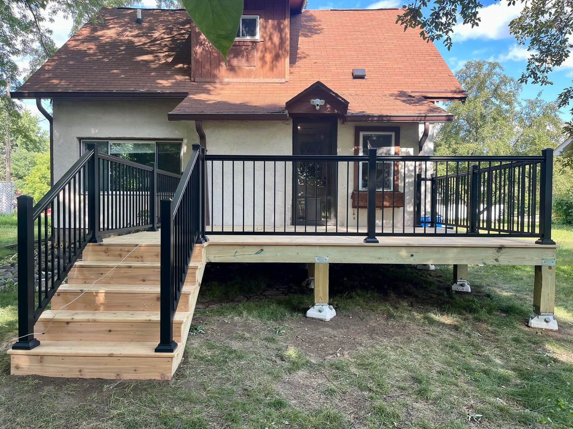 Small house with front porch deck, stairs, black railings, and a chair on the right side