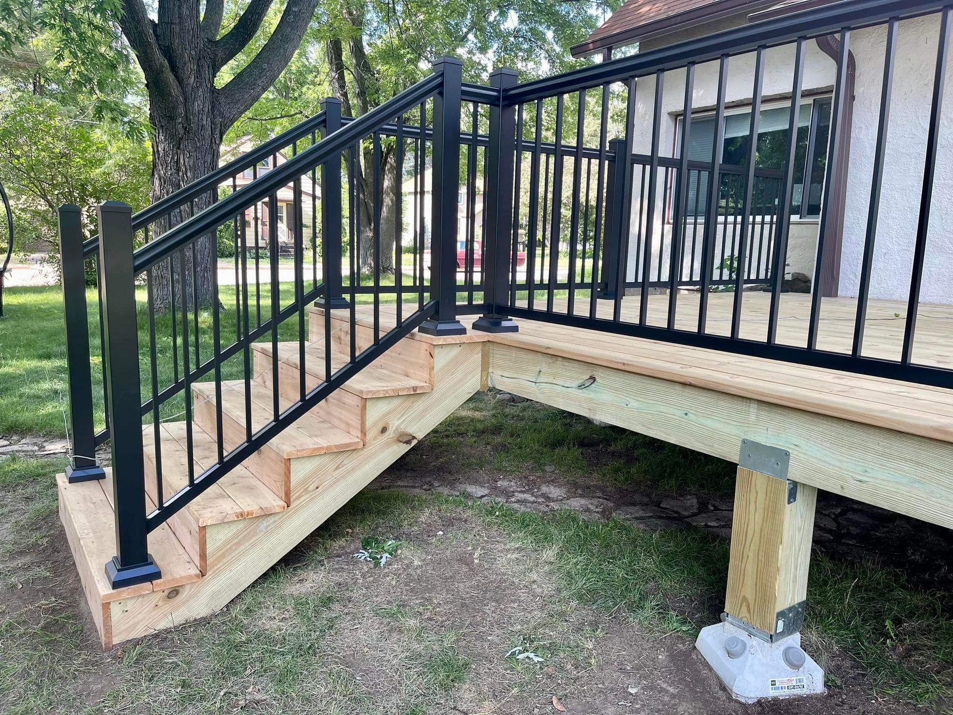 Black-railed wooden ramp leading to a house porch, with concrete supports and grassy yard below