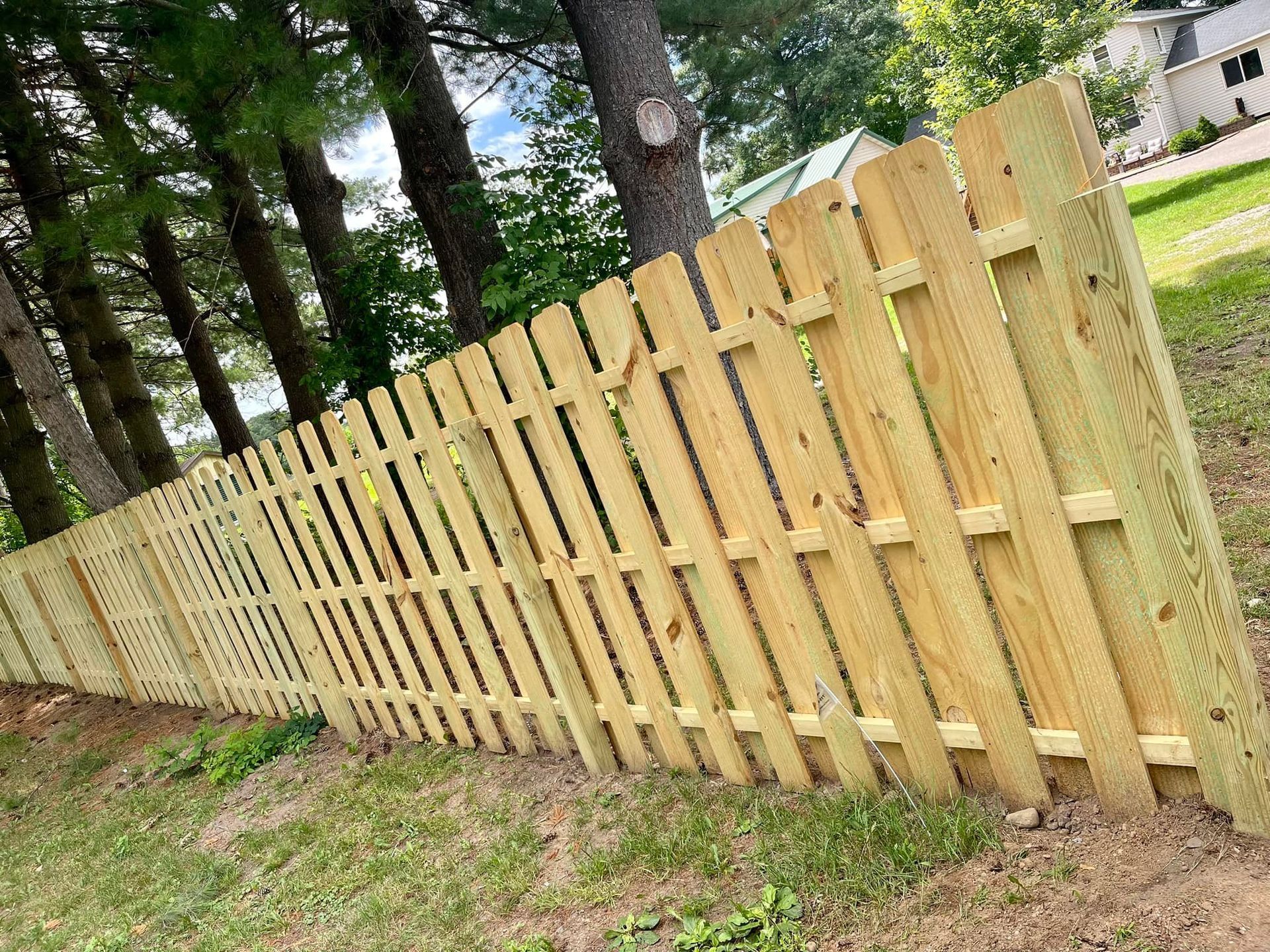 Wooden fence along a grassy yard beside tall trees, viewed at an angle