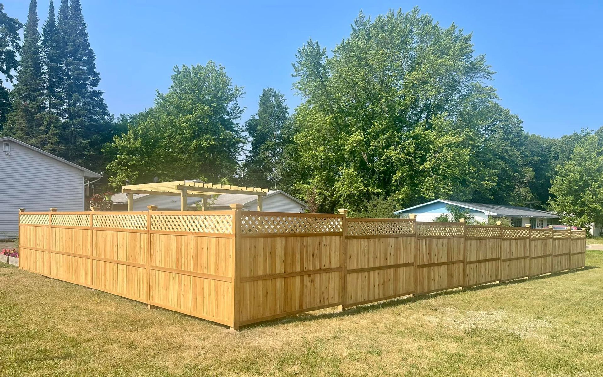 Large fenced wooden backyard enclosure under a sunny blue sky, with houses and trees in the background