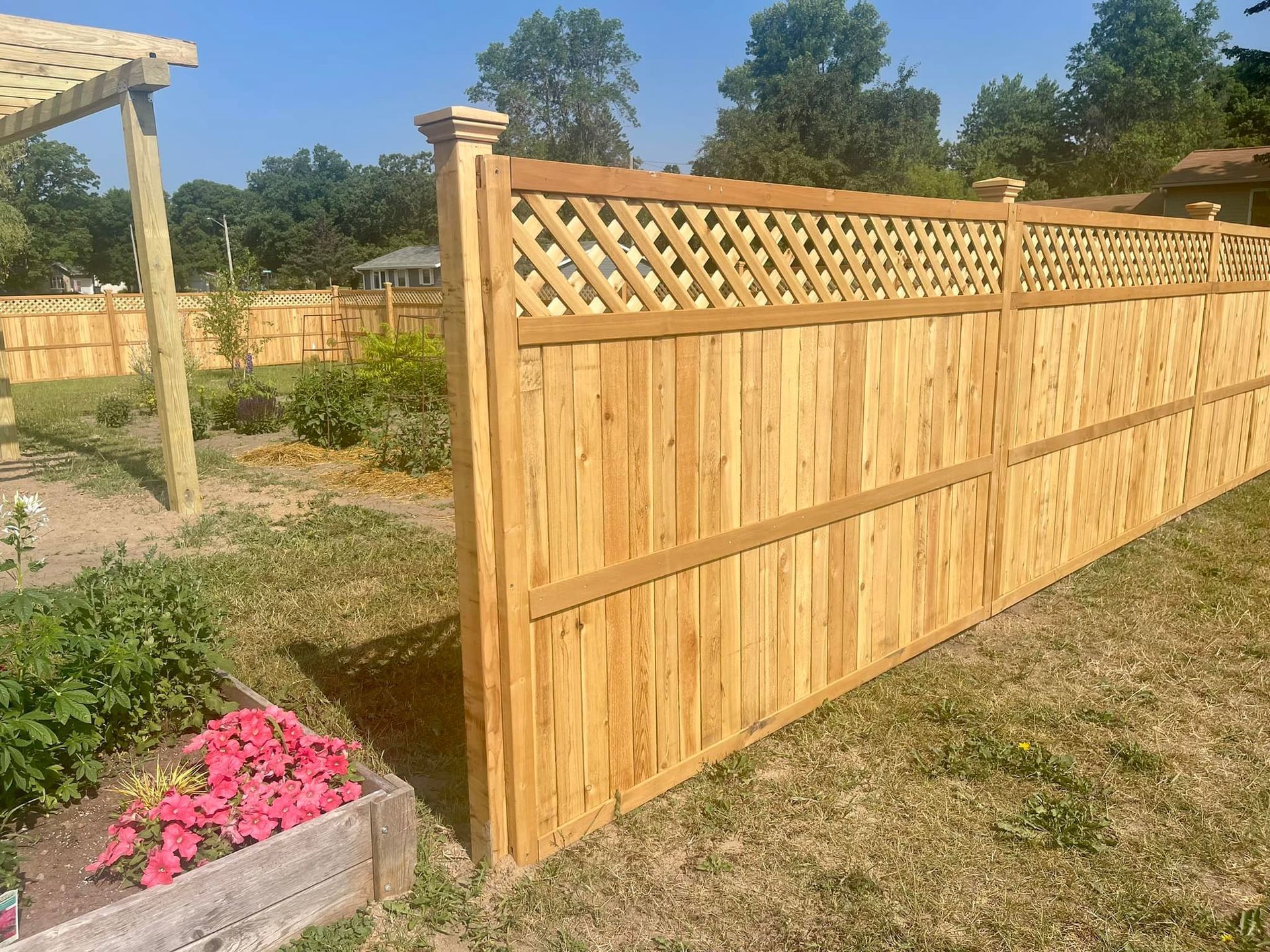 Wooden lattice-topped fence in a grassy yard with a small pink flower bed in the foreground.