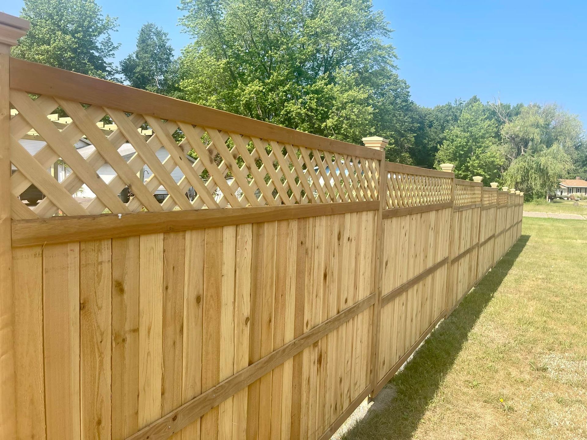 Wooden privacy fence with lattice top beside a grassy yard under a sunny sky