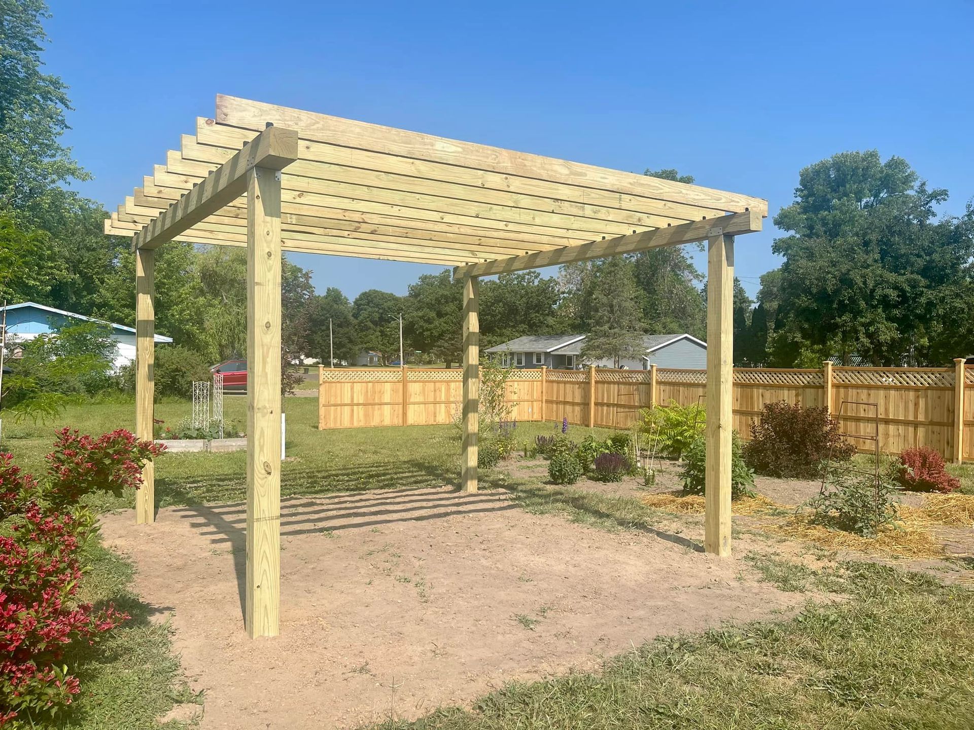 Wooden pergola in a landscaped backyard with gravel ground and a fenced garden.