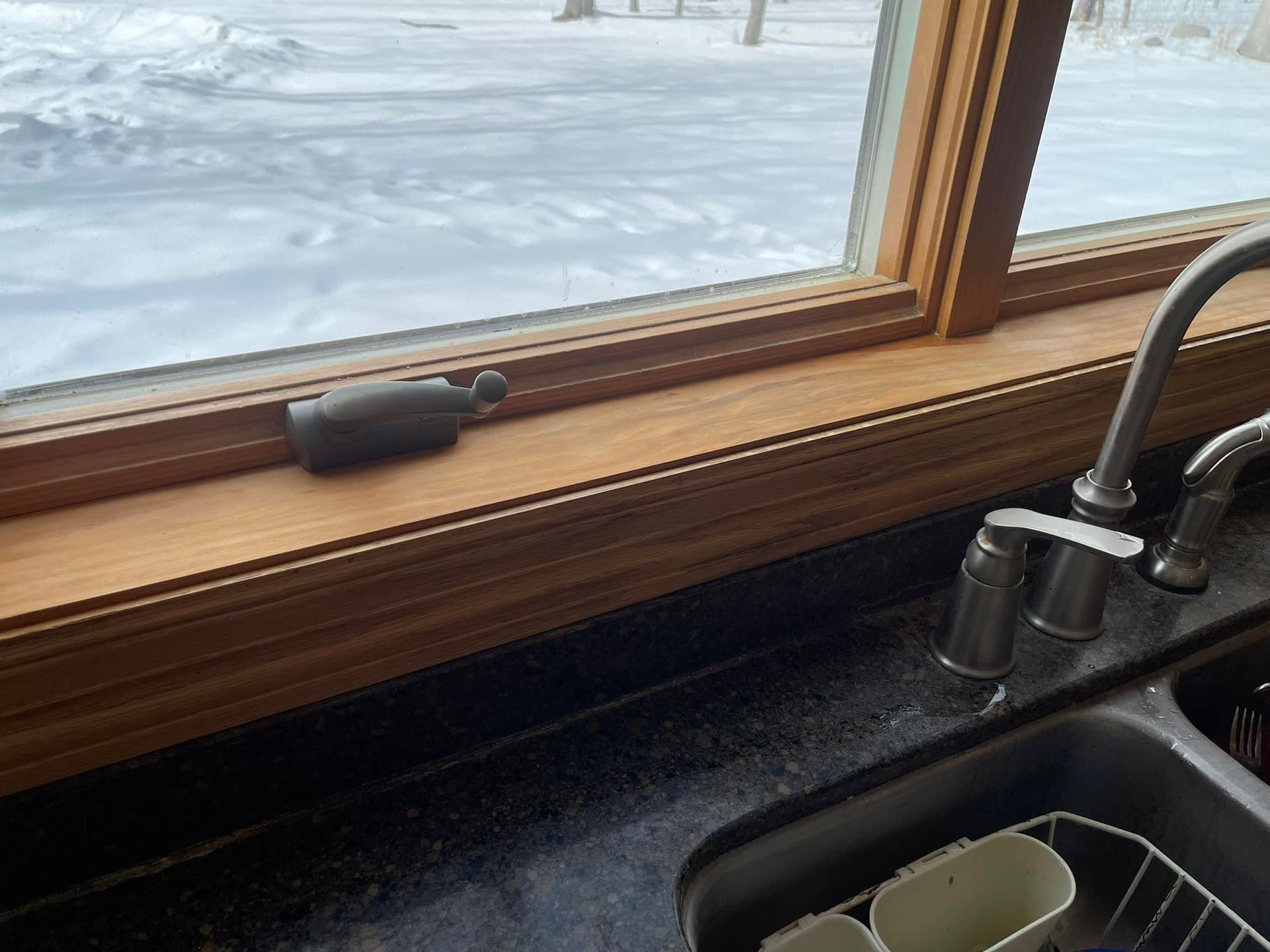 Kitchen sink and window with snowy outdoor view, wooden sill, and a soap dispenser on the counter.