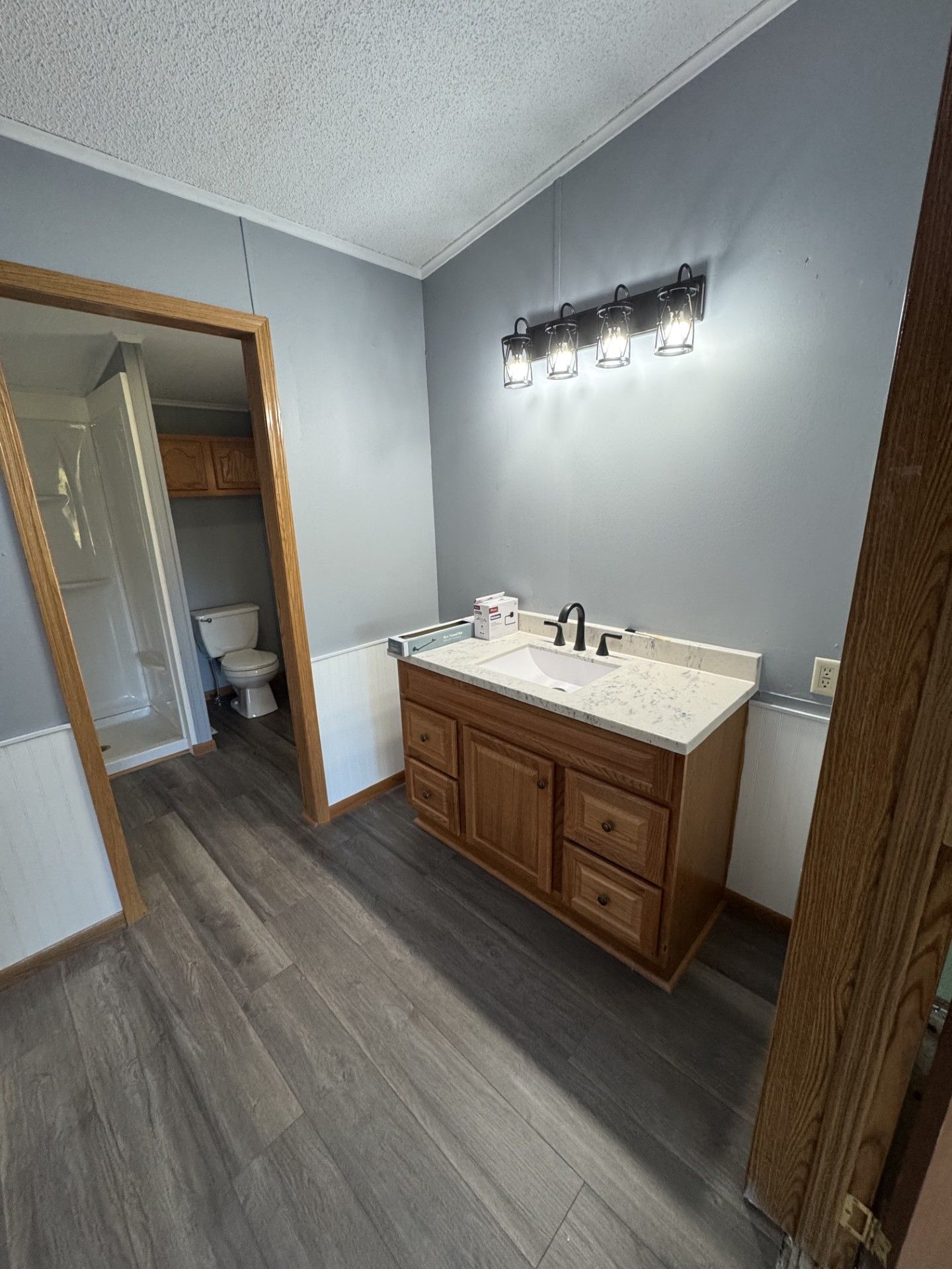 Bathroom with wood vanity, white sink, wall light, gray walls, and wood-look tile floor.