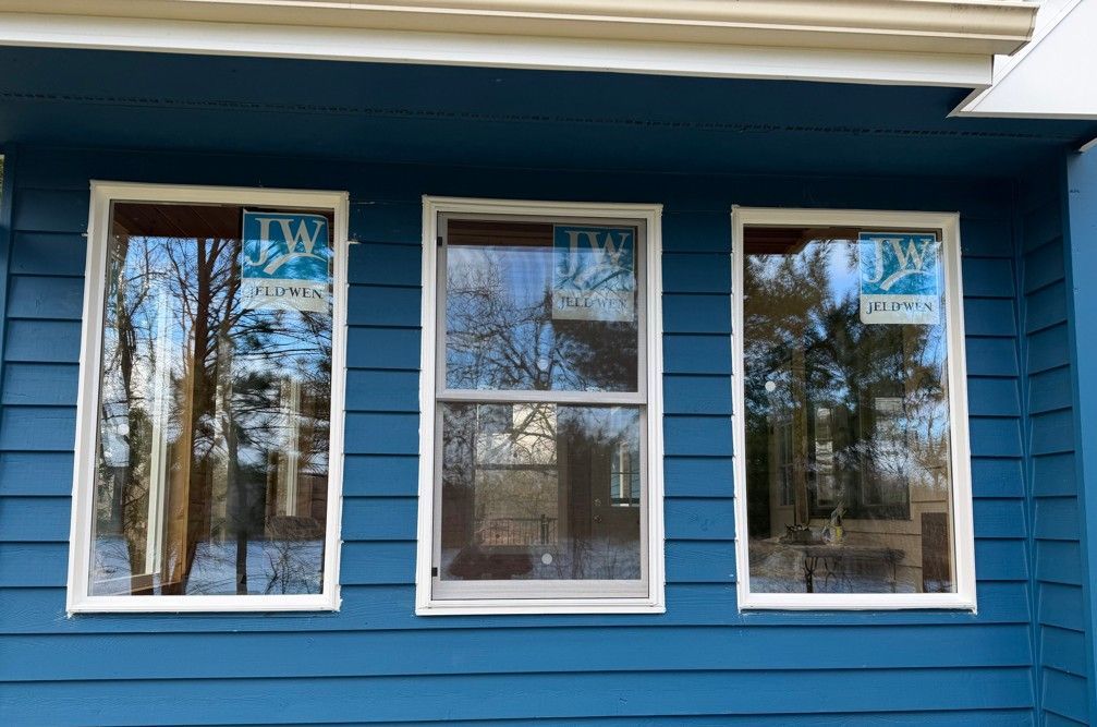 Three white-trimmed windows on a blue house exterior reflecting trees and sky